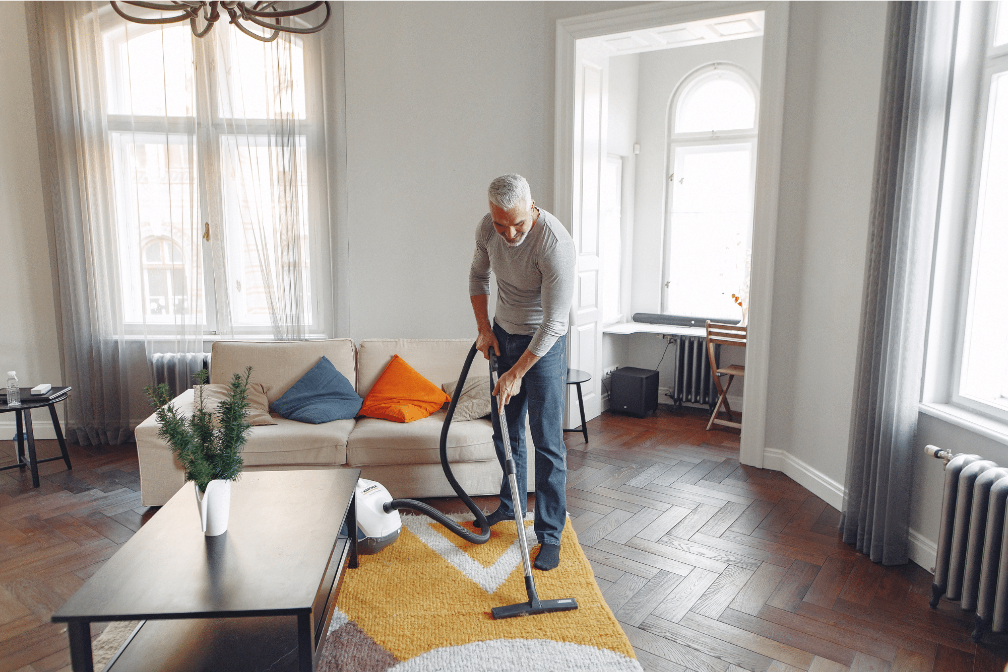 A man using a HEPA vacuum to clean a modern living room with hardwood floors and a stylish rug, enhancing indoor air quality