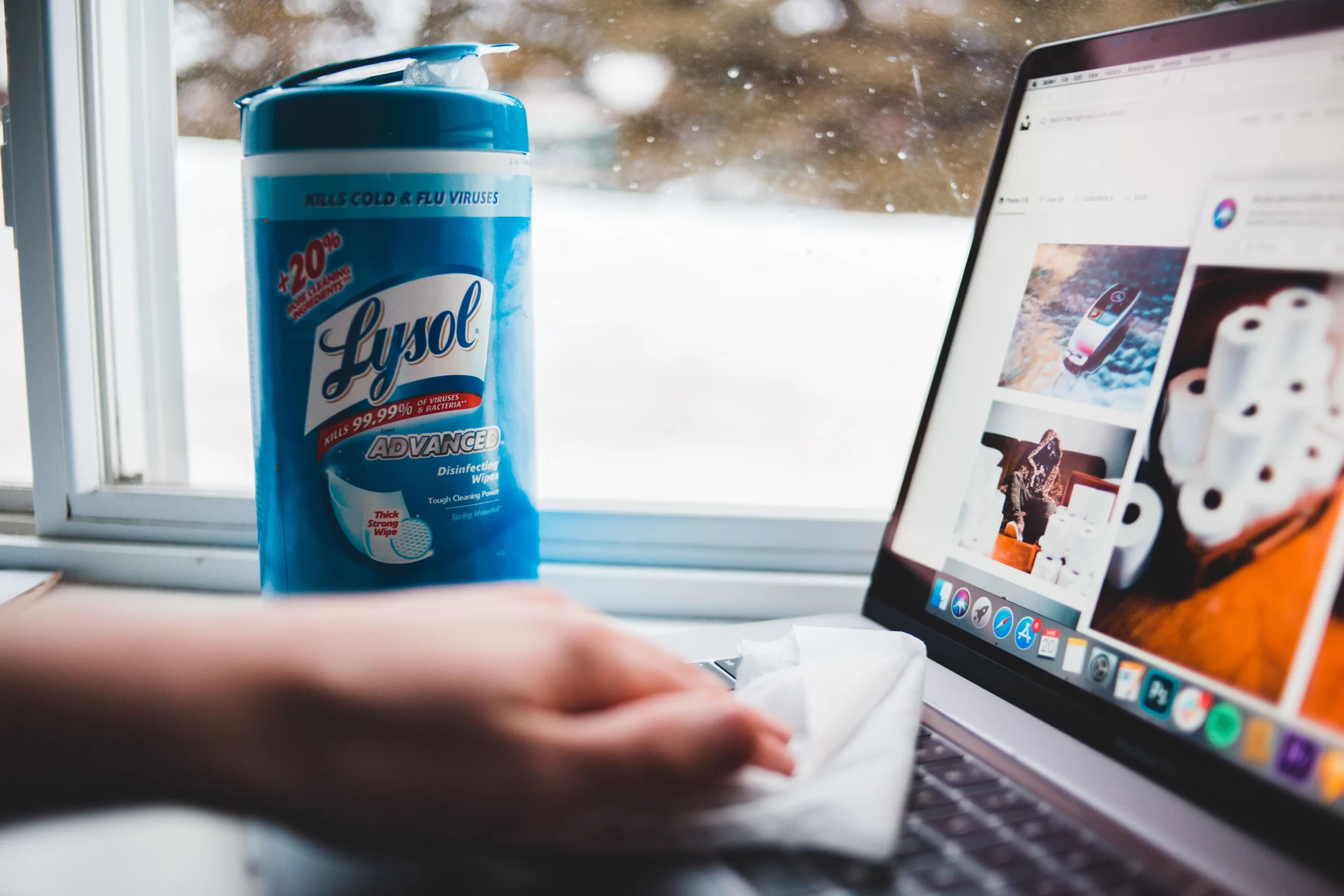 Does Lysol Kill Mold Effectively? A Quick Guide 1 A person using a Lysol disinfecting wipe to clean a laptop beside a window, representing the question does Lysol kill mold on surfaces.
