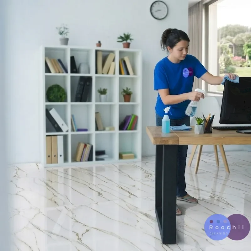 A young female Cleaner cleans a computer monitor in a modern office with polished white marble tile floors.